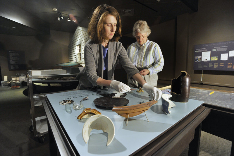 Kate McBrien and Linda Carrell arrange artifacts from Malaga Island for the exhibit “Malaga Island, Fragmented Lives” at the Maine State Museum in Augusta.
