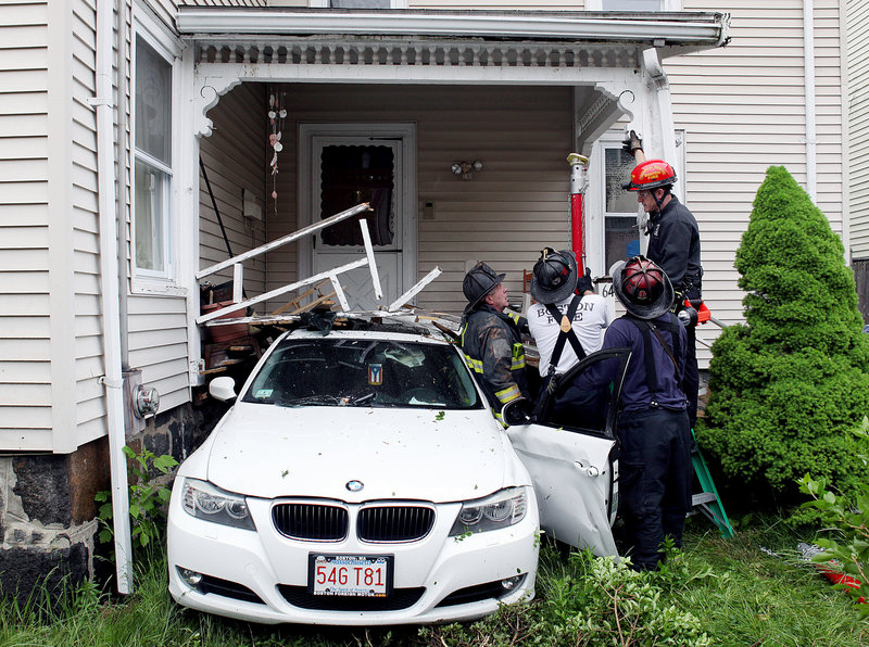 Boston firefighters work to support the porch of a home after an 8-year-old boy backed his mother’s BMW out of their driveway across the street and crashed it Wednesday. No one was hurt.
