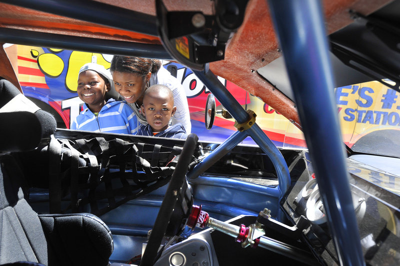 Evelyne Kanru of the Youth Outreach Family day-care program shows the interior of a race car to Noel, left, and Cedric. The cars in Monument Square in Portland on Friday were from Oxford Plains Speedway, which will be the site of an American Canadian Tour race Sunday.