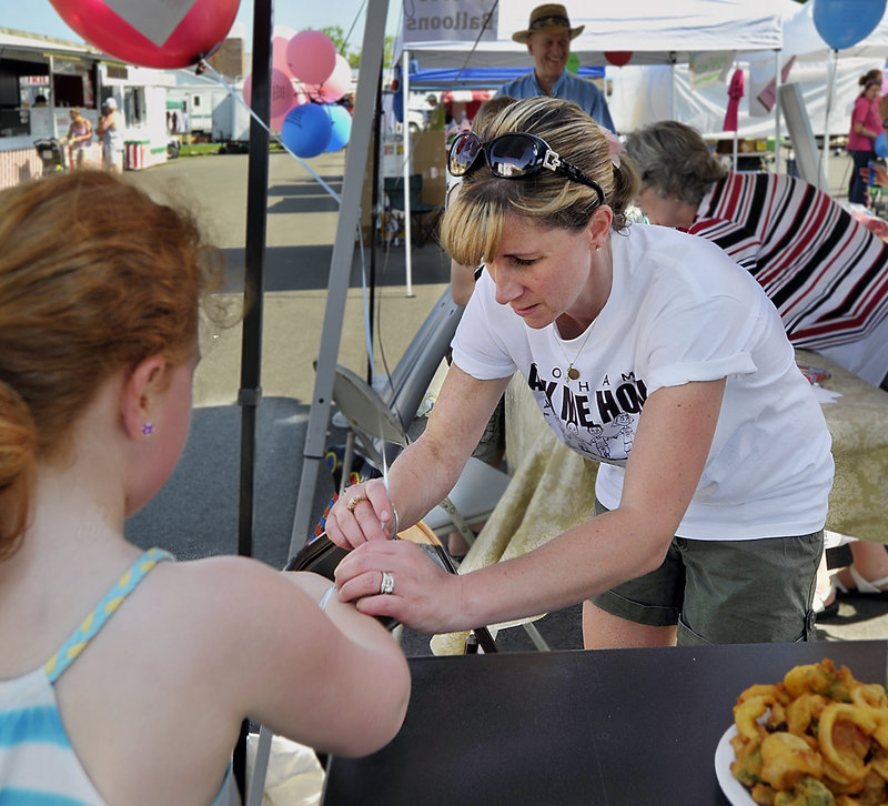 Kelli Deveaux ties a balloon to the wrist of a visitor as she works a booth at the Gorham Founder’s Festival where she promoted all-day kindergarten. The change would add an estimated $400,000 to next year’s school budget, and officials have said it’s not the right time to raise costs for taxpayers.