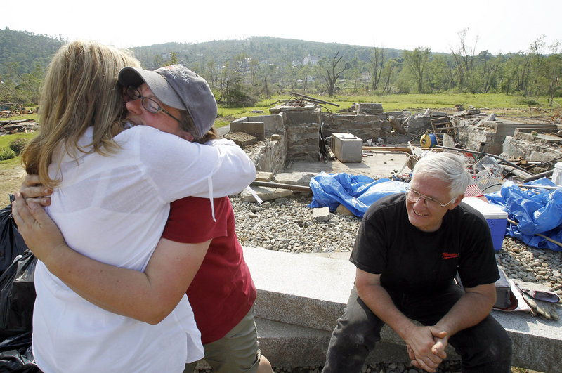 Diana Robbins, left, and Pia Rogers hug as Rogers’ neighbor Dwight Meacham sits in front of Rogers’ destroyed home last year after a tornado blew through Monson, Mass. The storm took a heavy toll, but it also brought people together to clear debris and weigh what to do next.