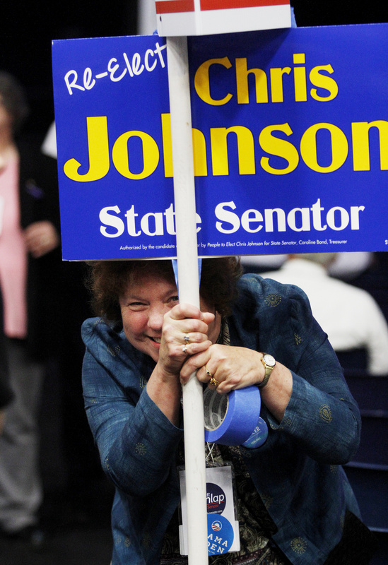 Sandra Farrell, treasurer of Lincoln County Democrats, peeks out while hanging a sign supporting the re-election of Sen. Chris Johnson.