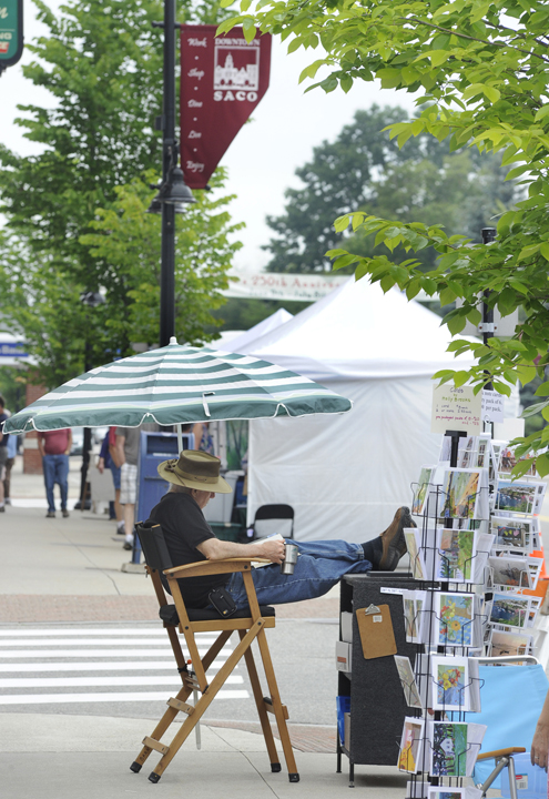 Artist Joseph Barnett from Kennebunk relaxes after setting up his display at Saco's 250th Anniversary Celebration sidewalk art show.