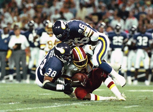 In this Aug. 29, 1992, file photo, Minnesota Vikings' Todd Scott (38) and Audrey McMillan (26) bring down Washington Redskins wide receiver Art Monk during an NFL football exhibition game in Washington. More than 60 former NFL players have filed a lawsuit in Los Angeles, joining hundreds of others who claim pro football didn't properly protect its players from concussions. Monk, the lead plaintiff, played for the Redskins from 1980 to 1993, and says in the lawsuit filed last week that he suffered multiple concussions in that time.