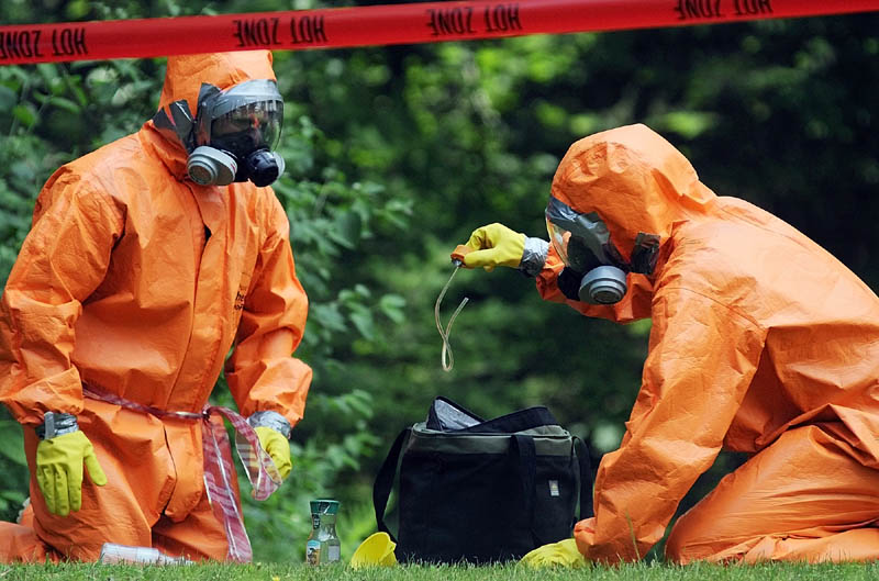 HOT ZONE: Maine Drug Enforcement Agents inspect items they collected Thursday behind a home on Cressey Road in Monmouth, where three men were arrested Wednesday during an investigation of an alleged methamphetamine lab. Agents donned hazardous material suits in 90 degree heat while collecting evidence at the trailer for several hours.