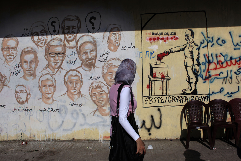 An Egyptian woman passes by a wall with graffiti depicting Egyptians killed during the revolution, left, and the military council casting a vote with a blooded hand and Arabic that reads "presidential elections 2012, down with Felol," in Cairo, Egypt. It's too early to say that Egypt's presidential election has redeemed the promise of last year's popular uprising against the country's authoritarian president, Hosni Mubarak.