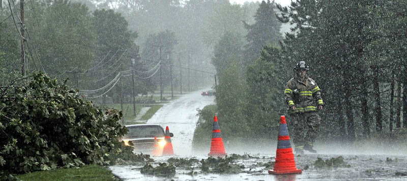A Fairfield firefighter sets up cones to redirect motorists around downed power lines and tree limbs from a powerful storm that rolled through central Maine on Friday afternoon.