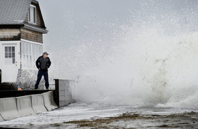 Bernie Malouin watches a large wave crash over Eastern Avenue at Camp Ellis in Saco from a wall in front of his cottage Monday.