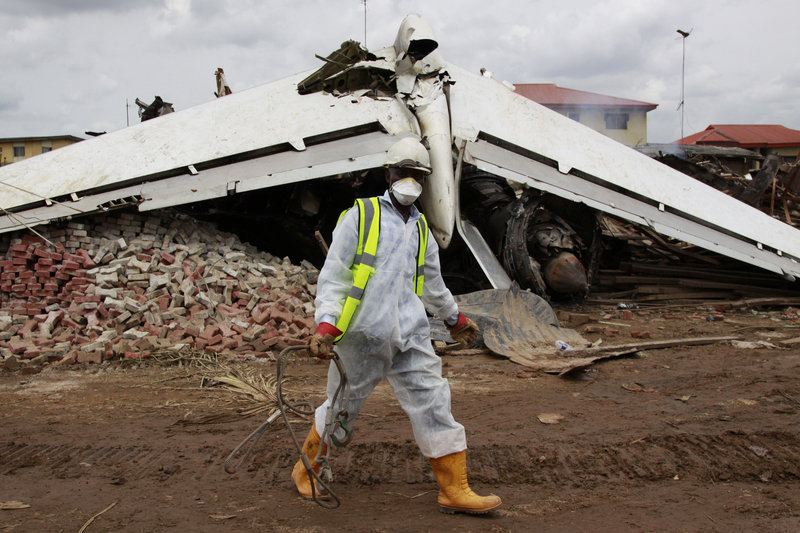 A rescue worker walks past the wreckage of a plane in Lagos, Nigeria, on Monday. The passenger plane carrying 153 people crashed in Nigeria’s largest city.