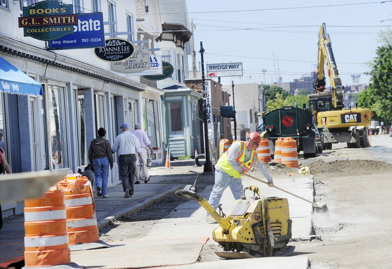 Mike Stuart of Shaw Brothers Construction cleans up in the construction zone Thursday as pedestrians walk along the sidewalk on Ocean Street in Knightville. The work began in April and is expected to continue through October.