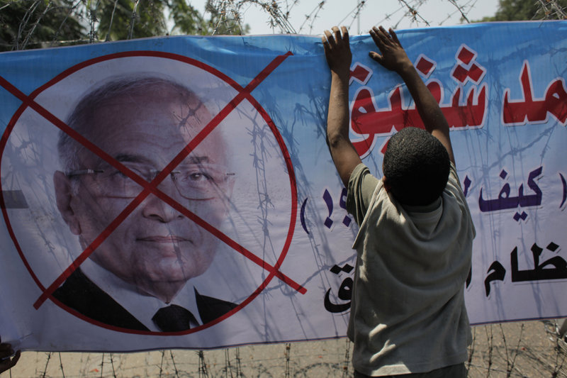 An Egyptian youth hangs a banner with a defaced picture of presidential candidate Ahmed Shafiq and Arabic that reads “Shafiq, the former regime,” in Cairo, Egypt, Thursday.