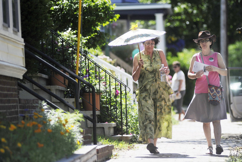 Ann Marie Knoepfel of Portland shades herself with a parasol as she makes her way down Morning Street with Kathleen Egan of South Portland. They were taking part in the Hidden Gardens of Munjoy Hill Tour on Sunday in Portland.