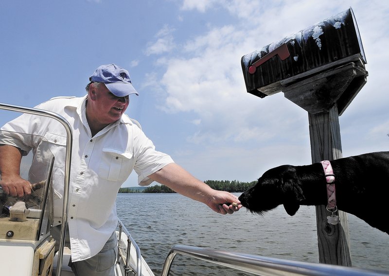 Norm Shaw gives a dog biscuit to a dog on mail route on Thursday in Belgrade. He has been delivering the mail from his boat on Great Pond in Belgrade and Rome for nine years.