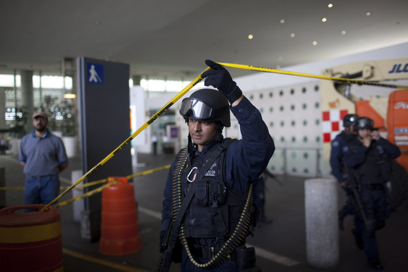 A federal police officer lifts a strip of crime scene tape as he leaves a marked-off area at Mexico City’s international airport, where three police officers were killed Monday.