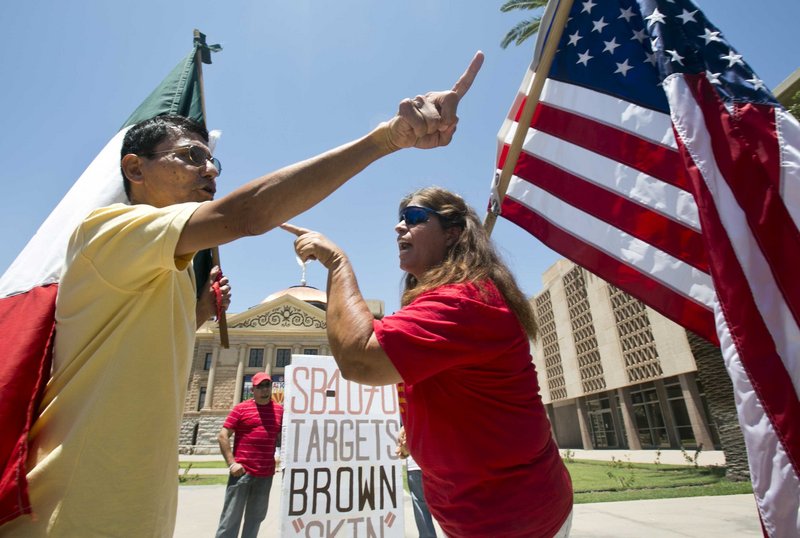 Andy Hernandez, carrying a Mexican flag, and Allison Culver, carrying an American flag, argue over Arizona’s immigration law outside the State Capitol in Phoenix on Monday. While finding parts of the Arizona law unconstitutional, the U.S. Supreme Court allowed the law’s most-discussed provision to stand.