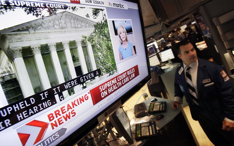 A television screen at a trading post on the floor of the New York Stock Exchange headlines the Supreme Court decision on health care Thursday.