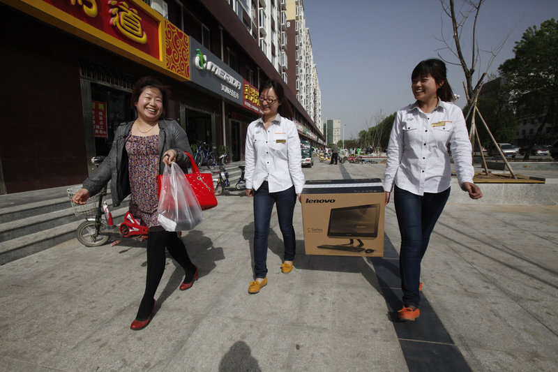 Two Lenovo sales associates carry a newly purchased white Lenovo All-in-One PC for Hou Yan Nan, 26, left, after she bought the computer in Da Shan, China.
