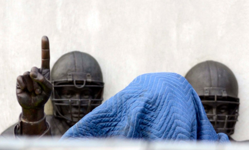 A covering lies on top of the head of the statue of former Penn State football coach Joe Paterno before it is removed today in State College, Pa. The famed statue of Paterno was taken down from outside the Penn State football stadium.