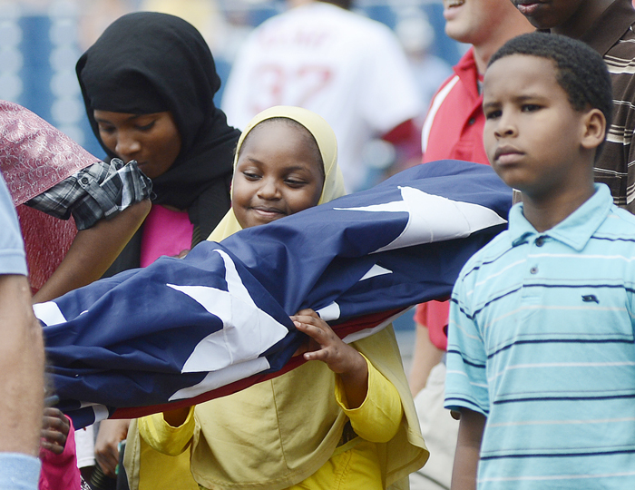 Samira Hassan, 8, of Auburn smiles as she carries the American flag on Hadlock Field for the singing of the national anthem prior to the start of the Portland Sea Dogs game today.
