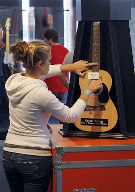 In this photo made on Tuesday, June 26, 2012, Courtney Dusseau, of Monroe, Mich., strums on an acoustic guitar strung with catgut strings that is part of the touring National Guitar Museum exhibit on display at the Carnegie Science Center in Pittsburgh, through Sept. 30, 2012. The National Guitar Museum is a traveling guitar museum searching for a home. Museum director HP Newquist said the initial plan was to take it on the road for five years, to find out which city was the most hospitable. The museum is on a nine-city tour. (AP Photo/Keith Srakocic)