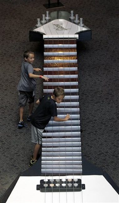 In this photo made on Tuesday, June 26, 2012, 10-year-old Ian Solorzano, bottom, and his brother Logan Solorzano, 8, play with the strings on the neck of the 40-foot long working model of a 1957 Gibson Flying V electric guitar that is part of the touring National Guitar Museum exhibit on display at the Carnegie Science Center in Pittsburgh, through Sept. 30, 2012. (AP Photo/Keith Srakocic)