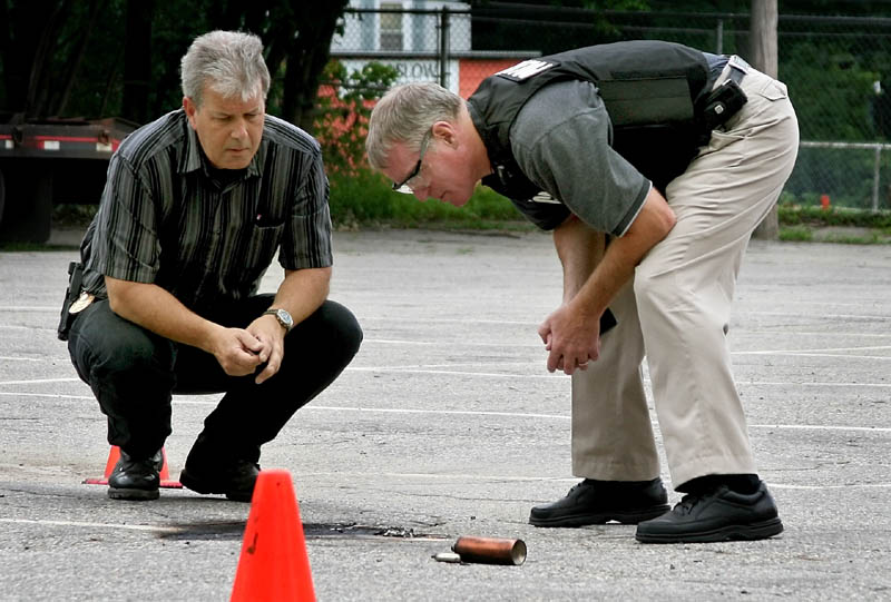 Winslow Police Chief Jeffrey Fenlason, left, and State Fire Marshal supervisor Ken Grimes examine the remains of an exploded device in the Winslow Junior High School parking lot Thursday. It was the third device exploded in Winslow in the last three days.