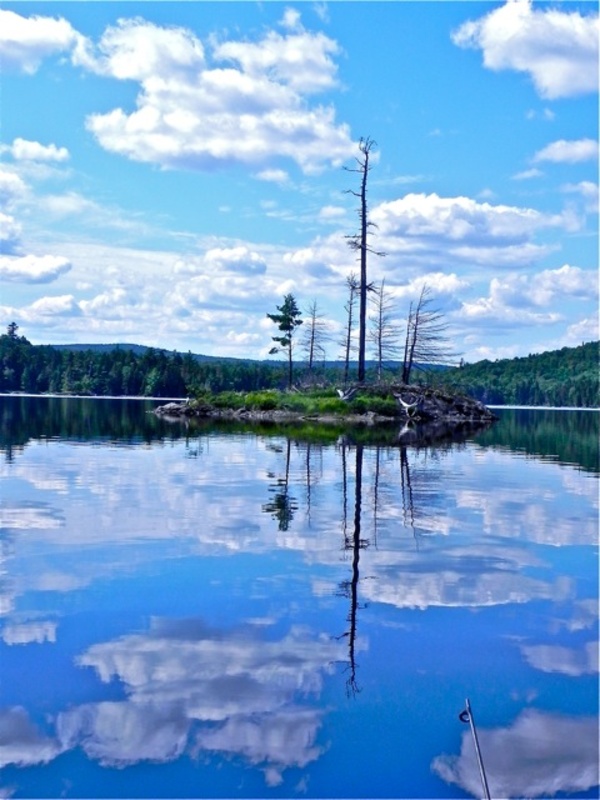The water mirrors the sky and small islands abound on a perfect day for canoeing in Maine.