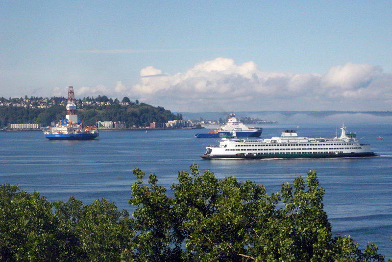 Ships carrying oil drilling equipment to Alaska, top, pass through Elliott Bay as a Washington State Ferry cruises into Seattle in June. While drilling must halt by September in the Chukchi Sea and by October in the Beaufort Sea to avoid the advance of sea ice, Shell Alaska’s barge is stuck in Washington state awaiting Coast Guard approval.