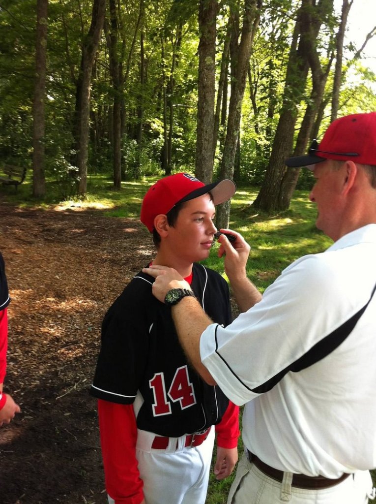 Scarborough Manager Neal Pratt applies eye black to catcher Owen Garrard before a game in South Portland. The team calls itself Eye Black because they all play with black triangles under their eyes, imitating the style of major league baseball star Bryce Harper.