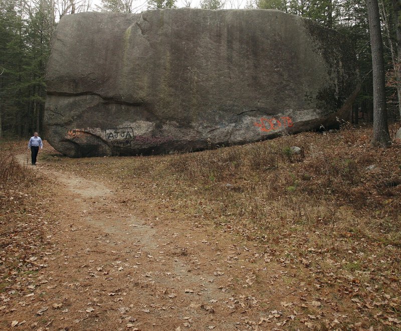 The Madison Boulder towers over state Rep. Jeffrey St. Cyr as he walks a path at its Madison, N.H., site. The boulder is the largest-known glacial “erratic” rock in New England, carried during the last ice age over mountains before breaking off here.