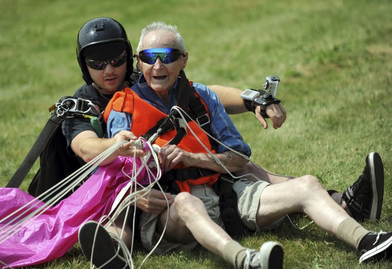Ninety-year-old Lester Slate of Exeter sits on the ground Sunday after his first skydiving jump made in tandem with instructor Matt Riendeau, left, at Central Maine Skydiving in Pittsfield. The jump, witnessed by about 50 family and friends, was a birthday present to himself.