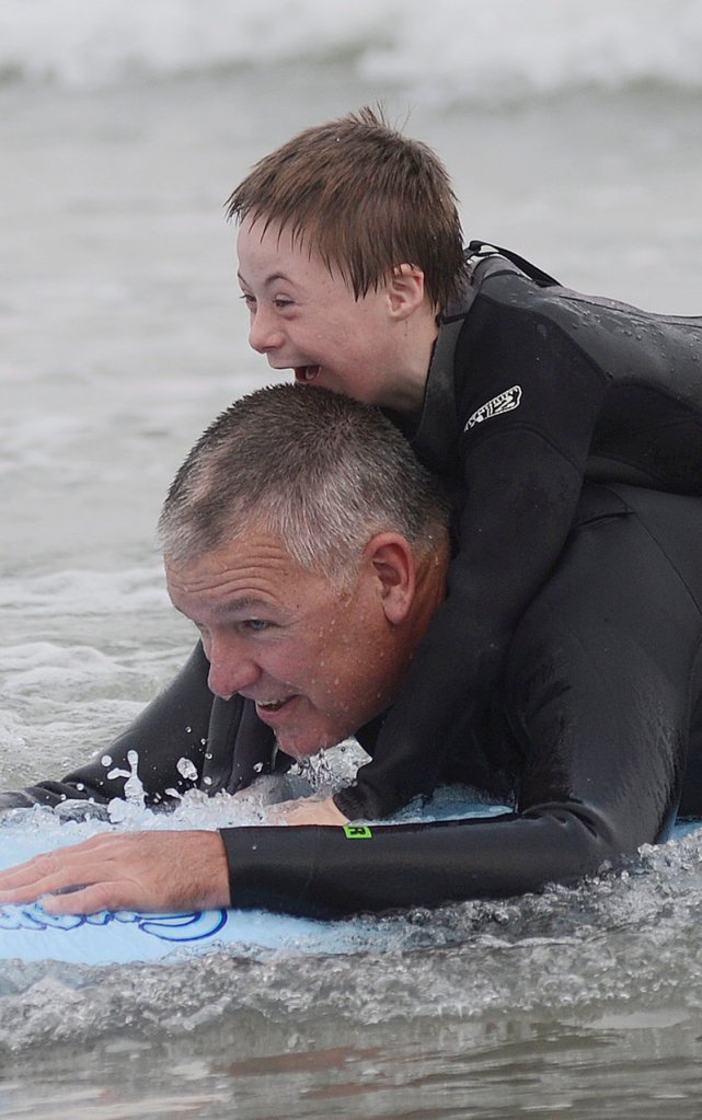 Eight-year-old Hunter Frechette of Biddeford is all smiles as he rides a wave on a surfboard while holding on to volunteer Marc Boutet of Saco during Special Surfer Night at Gooch's Beach in Kennebunk Tuesday.
