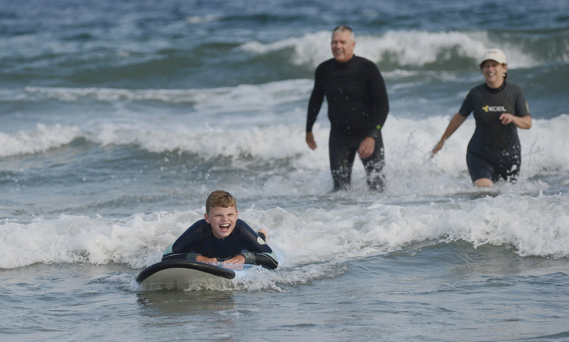 E.J. Marrifield, 9, of Belfast enjoys a ride on a surfboard during Special Surfers Night in Kennebunk on Tuesday. Looking on are volunteers Marc Boutet of Saco and Lynne Ableson of Kennebunk.