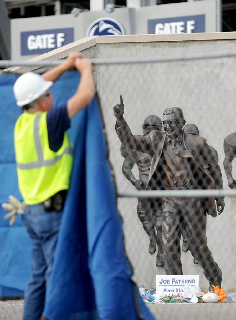 A worker hangs a tarp over a fence as crews work to remove Joe Paterno’s statue at State College, Pa., on Sunday. The university removed the monument in the wake of an investigative report that found that the late coach and three top Penn State administrators concealed sex abuse claims against Jerry Sandusky, who was convicted last month of sexually abusing 10 boys.