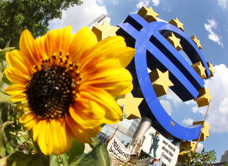 A sunflower sprouts beneath a sculpture of the euro in Frankfurt, Germany, but Europe’s economic status is now clouded by looming shadows of debt.