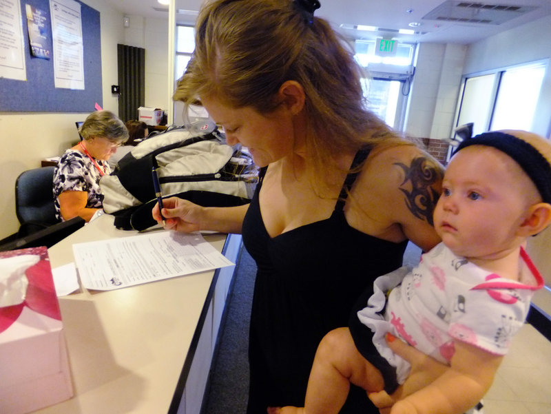 Laura Fritz, 27, with her daughter, Adalade Goudeseune, fills out a form at the Jefferson Action Center, an assistance center in Lakewood, Colo. Fritz grew up in a wealthy family, but she and her boyfriend, who has struggled to find work, are relying on government aid to cover food and $650 rent.
