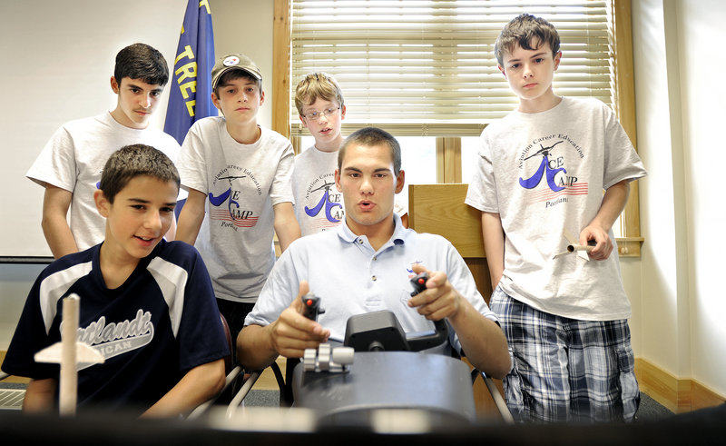 Levi Swan, 19, of Caribou, a maintenance crew chief with the Air National Guard, demonstrates a flight simulator for campers Thursday at the Aviation Career Education camp at the Boy Scouts’ conference facility near the Portland Jetport.