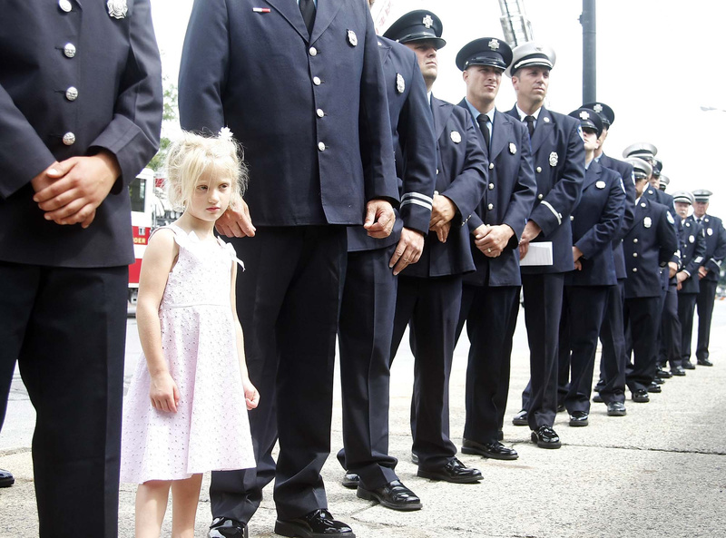 Melina Slaving, 4, of Old Orchard Beach stands with her father, Lt. Robert Slaving, as he waits with fellow firemen to read off names of the fallen firefighters at the Portland Fire Department Fallen Firefighter Memorial Dedication at Central Fire Station in Portland on Saturday.