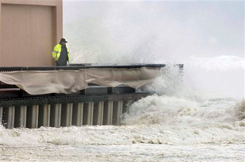 An unidentified Okaloosa County Deputy Sheriff stands next to the Jetty East condominium in Destin, Fla., Tuesday, Aug. 28, 2012 as a wave crashes over the buildings boardwalk. Although Isaac is expected to make landfall in Louisiana, the storm still pounded shorelines along Northwest Florida as it moved through the Gulf of Mexico. (AP Photo/Northwest Florida Daily News, Devon Ravine)