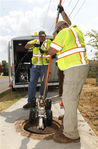 Derek Johnson, left, environmental unit supervisor, and Jeff Everett, right, an environmental technician from Oklahoma City's Storm Water Quality division of Public Works, lower a video camera into a storm drain in Oklahoma City recently to look for evidence of mosquitoes,
