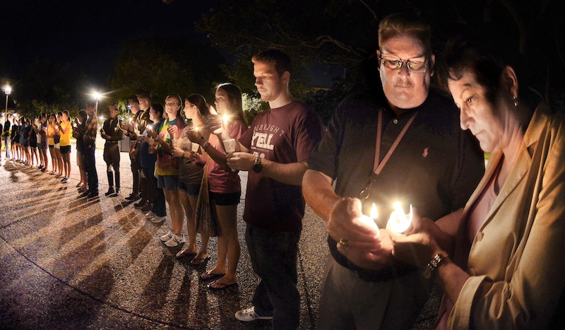 In this Monday, Aug. 13, 2012 photo, Texas A&M chief of police Elmer Schneider, right, gives his wife Dee Ann a flame from his candle during the candlight vigil on the Texas A&M campus in College Station, Texas. Police said Tuesday that 35-year-old Thomas Alton Caffall III had "long guns and pistols" in his home when Brazos County Constable Brian Bachmann showed up to deliver an eviction notice. Officials say Bachmann was fatally wounded as he approached the home and a bystander died in the shootout. Caffall died at a hospital. (AP Photo/Bryan-College Station Eagle, Dave McDermand)