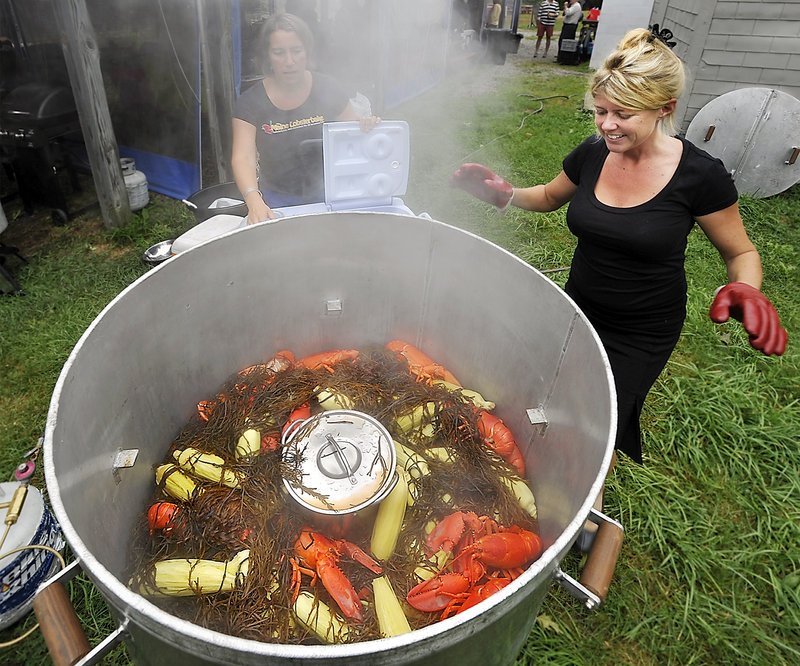 Courtney MacIsaac, right, is the owner of the Maine Lobsterbake Co., which caters a lot of corporate events and wedding-related gatherings. She and server Cheryl Scribner-Rocha survey a steamer filled with lobsters and corn at a recent bake on Peaks Island.