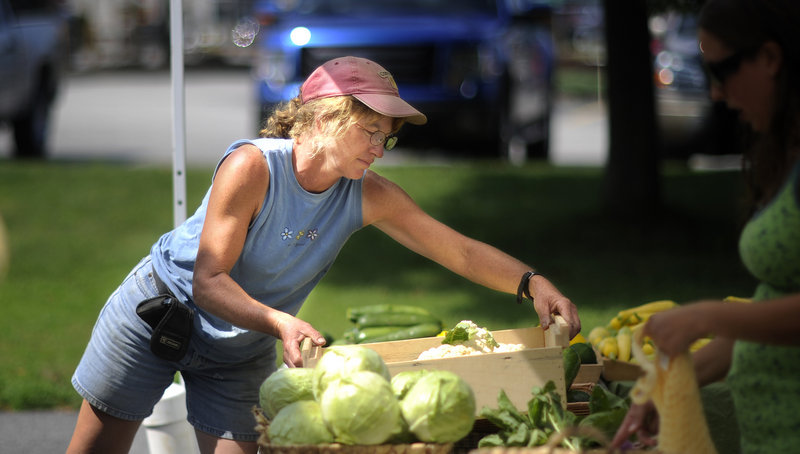 At top, Cathy Karonis of Fairwinds Farm in Topsham prepares produce at the marketplace on Thursday. While Karonis says she believes there is a potential customer base to be tapped into in South Portland, two vendors have left the market because of low customer counts.