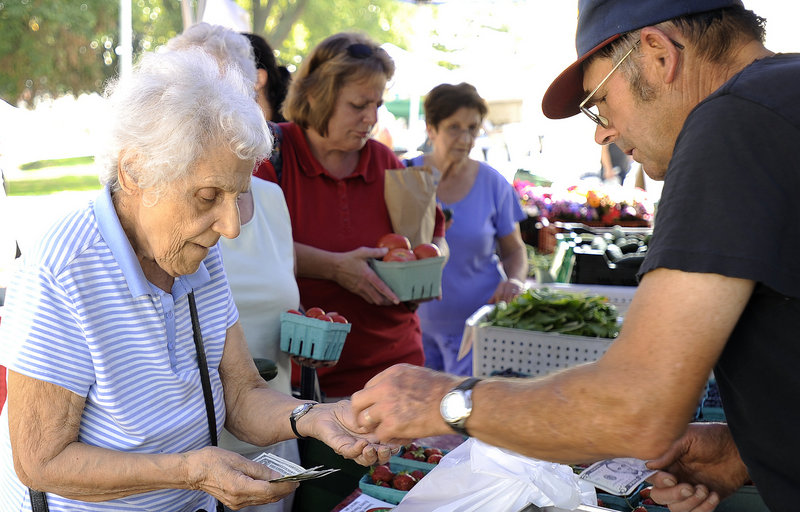 Kareemi Atallah, left, 93, of South Portland, buys produce Thursday from Jodi Jordan of Alewive’s Brook Farm at the South Portland Farmers Market. Vendors at the Hinckley Drive site want to encourage more customers like Atallah, who says she shops at the market every week.