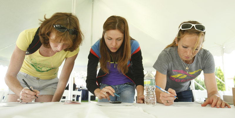 Three elite runners, left to right, Kseniya Agafonova and Valentina Galimova of Russia and Esther Erb of the U.S. fill out their registration forms for Saturday’s TD Beach to Beacon 10K.