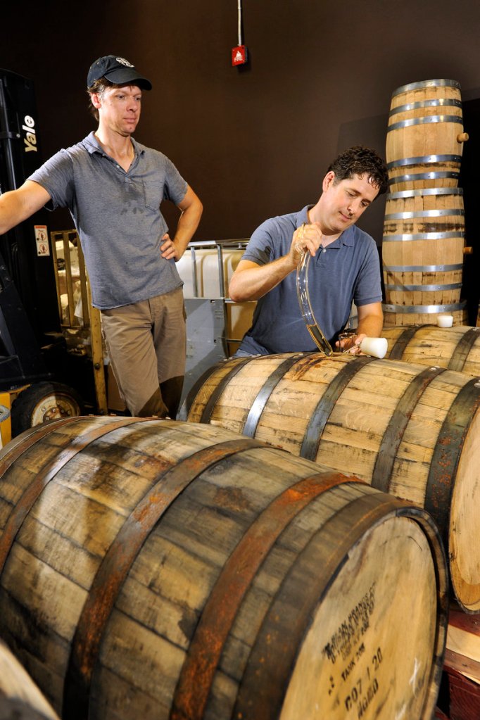 Distiller Tim Fisher, left, watches as Ned Wight uses a “barrel thief” to sample a batch of rum.