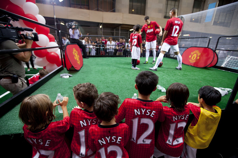 Children gather to watch Manchester United performers outside the New York Stock Exchange on Friday. The soccer club is the best-known sports team in the world, but its finances are less sterling: It is hundreds of millions of dollars in debt.