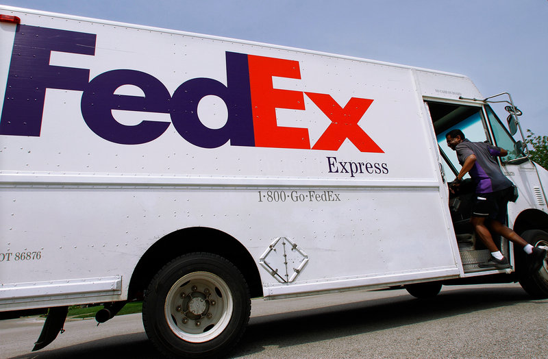 A FedEx employee climbs aboard a delivery truck as he makes his rounds in Springfield, Ill. FedEx said Monday it will soon begin offering buyouts to U.S. employees in an effort to cut costs.