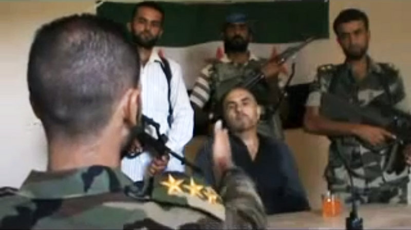 Image made from amateur video purports to show Syrian Col. Rafik Mohammed Suleiman being interrogated by a rebel officer after his Soviet-made MiG warplane was apparently hit by ground fire over Deir el-Zour province.