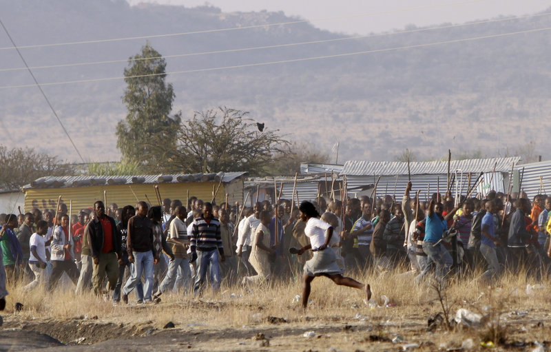 A woman runs in front of striking mine workers during tense moments at the Lonmin mine near Rustenburg, South Africa, on Friday. Some miners vowed a fight to the death Friday as police announced the death toll of 34 from the previous day.